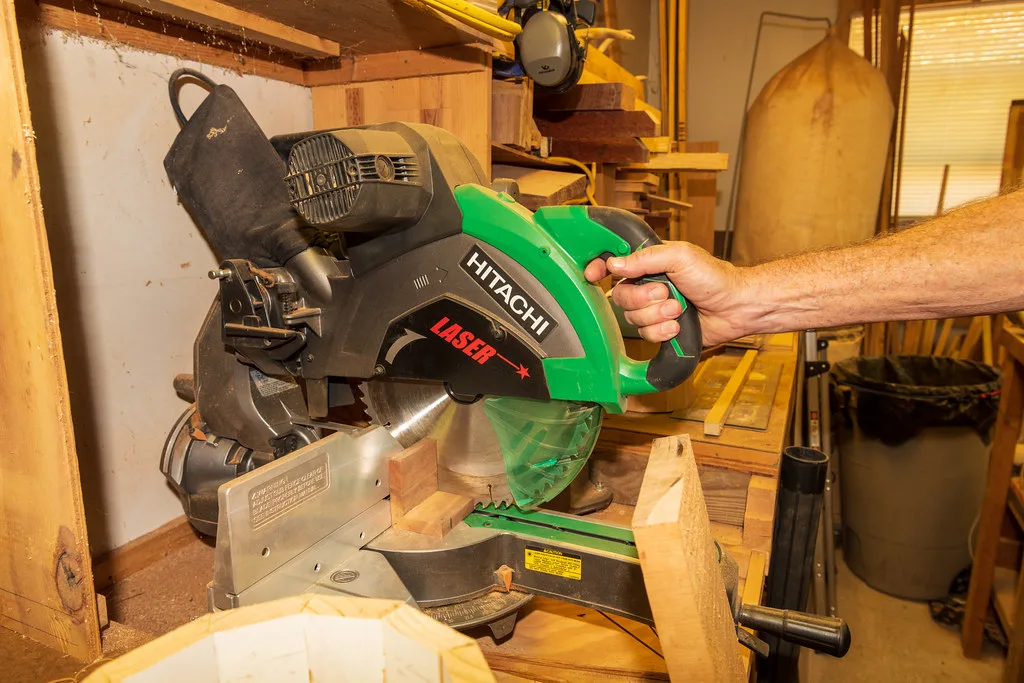 A sliding compound miter saw with its arm pulled out, the blade positioned over a long board on a wooden workbench.